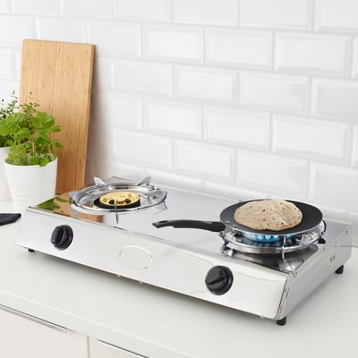 A portable gas stove with two burners. One burner has a pan with flatbread cooking, the other holds a covered dish.