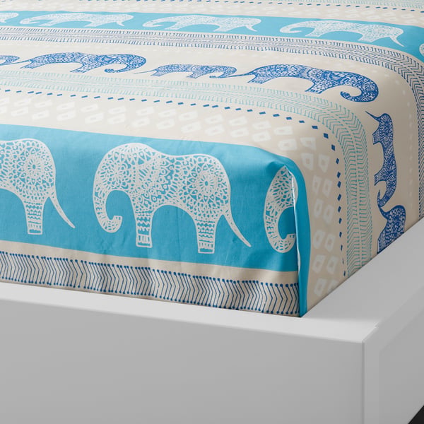 A colourful bedspread with large, patterned elephants in shades of blue and white on a beige background.