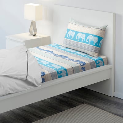 Bed with white and blue elephant bedding, including fitted sheet, pillowcase, and white lamp on bedside table.