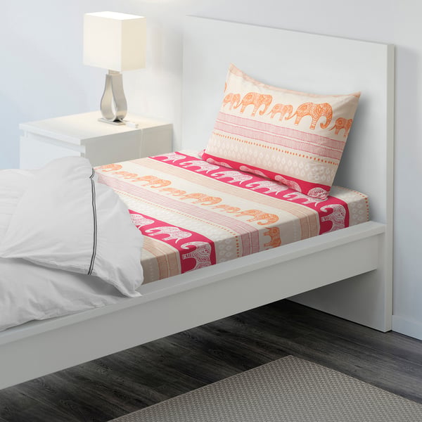 A white twin bed with a colourful elephant-patterned bedsheet and matching pillow, featuring a stylish white lamp on the bedside table.