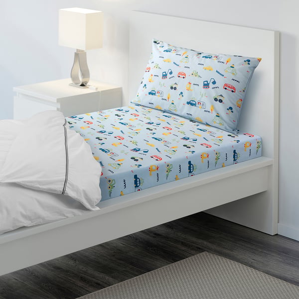 Light blue BARNDRÖM bedding with vehicle prints, cotton/viscose, fitted sheet and pillowcase, small bed setup next to a table with a lamp.