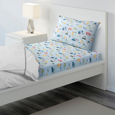 Light blue BARNDRÖM bedding with vehicle prints, cotton/viscose, fitted sheet and pillowcase, small bed setup next to a table with a lamp.