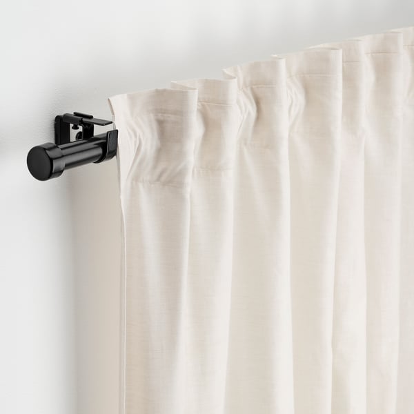 White curtains hang from a black BEKRÄFTA rod set, including holders and connectors.