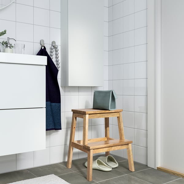Bathroom with BEKVÄM step stool, light wood, simple design, small size fits in corner, white towel hanging nearby.