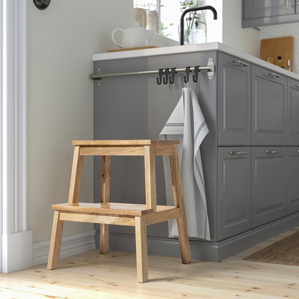 Wooden BEKVÄM step stool, mango wood, rectangular with handle, next to dark cabinets.