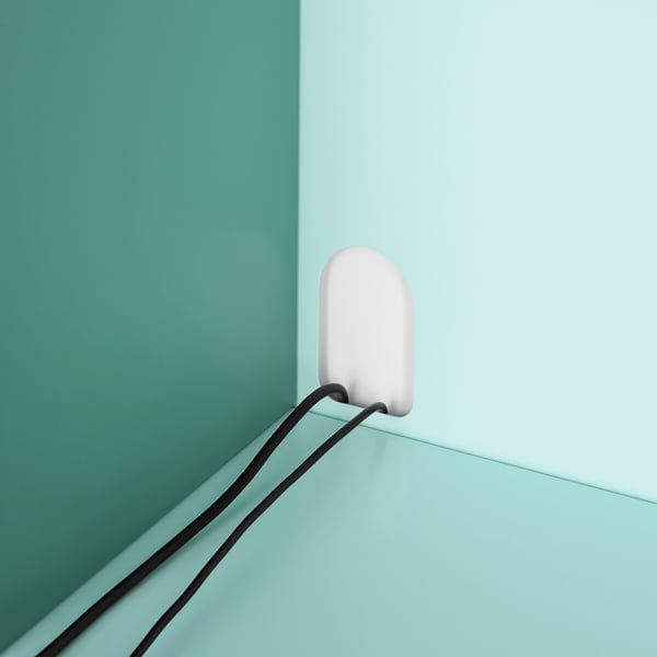 A pastel pink lamp hangs at an angle on a mint green wall, connected by a black cord, showcasing minimalist design.