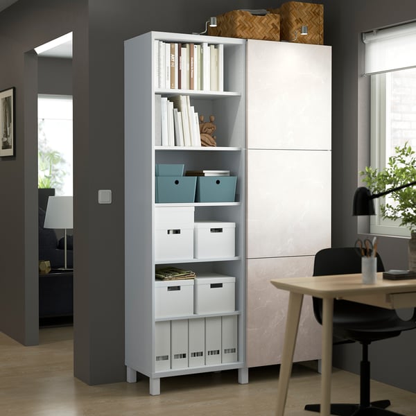 White BESTÅ storage unit with open shelves, books, and boxes near a desk.
