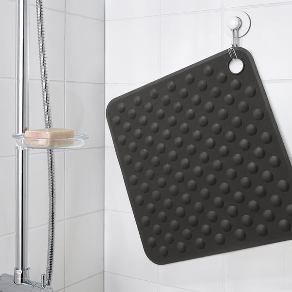 Black bath mat with suction cups hangs on wall.