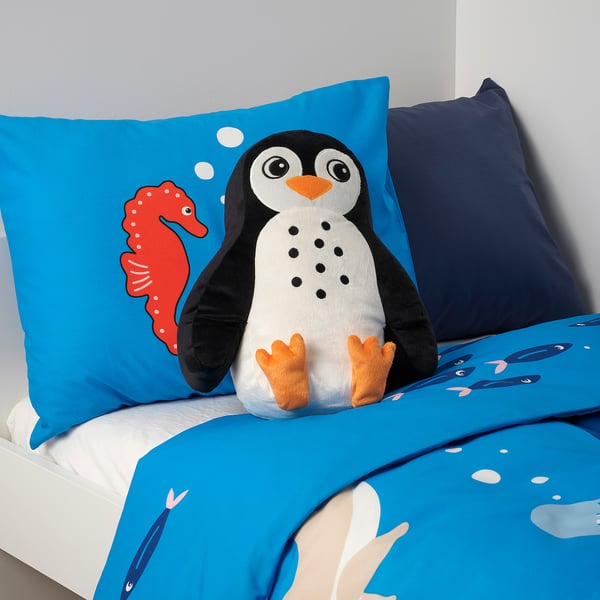 Penguin cushion on bed with whale & fish prints.