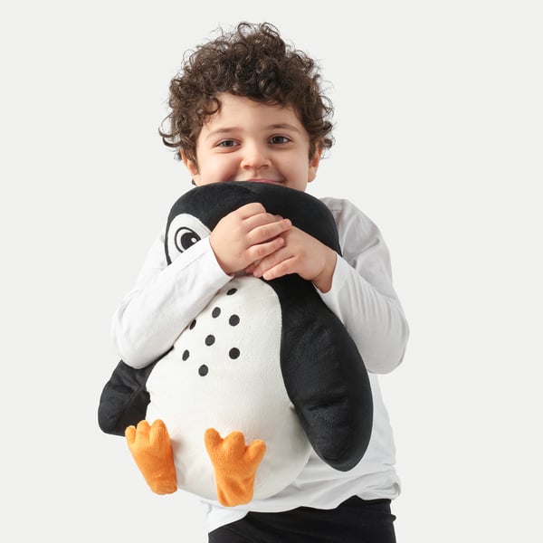 Boy hugs soft penguin pillow with black spots and orange feet.