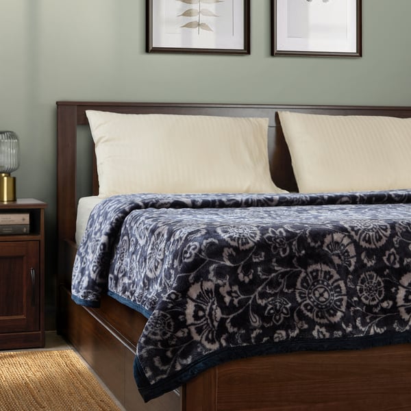 Dark blue floral blanket on wooden bed with cream pillows, side lamp.
