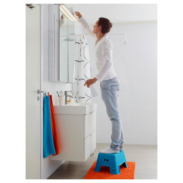 Person standing on blue step stool, adjusting bathroom cabinet mirror.