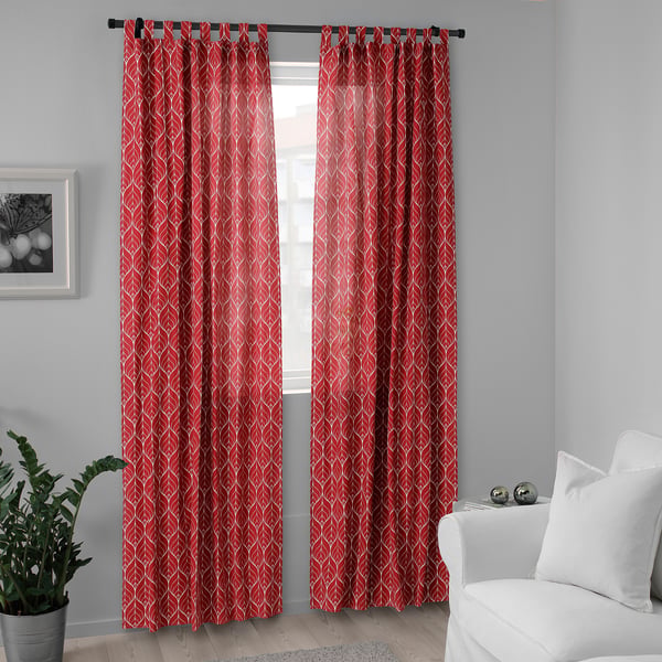 Bright red BRITTKARIN curtains with white patterns hang by a window, complementing a white chair and a small potted plant.