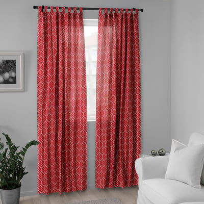 Bright red BRITTKARIN curtains with white patterns hang by a window, complementing a white chair and a small potted plant.