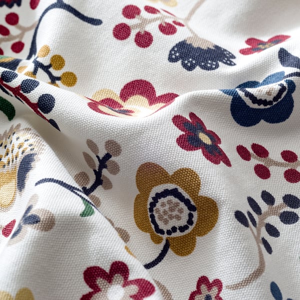 Close-up of vibrant, detailed floral-patterned white fabric. Flowers in red, yellow, and blue; intricate, high-quality design.