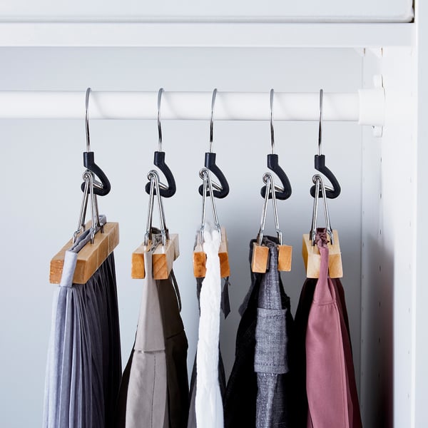 Black hangers with wooden clips holding trousers, keeping them neat and organised.