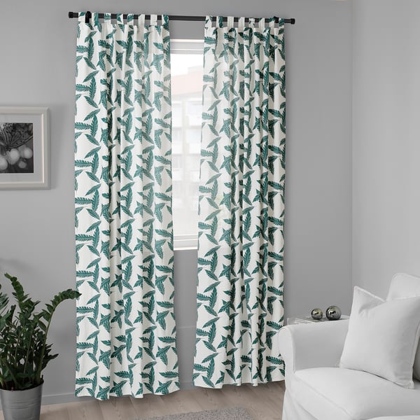 White curtains with leaf patterns hang over a window, appearing tall and wide, covering it almost entirely.