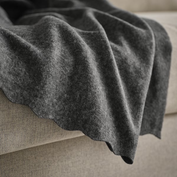 Dark grey fleece blanket draped on a beige couch, showcasing its soft and cosy texture.
