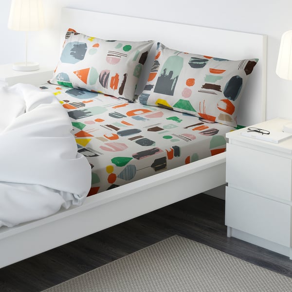 Colourful bedding set with abstract patterns, two pillows, on a white bed frame, in a minimalist room.