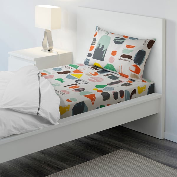 Bed with colourful, abstract print sheets and white pillows. Lamps on bedside table.