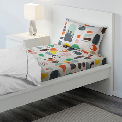 Bed with colourful, abstract print sheets and white pillows. Lamps on bedside table.