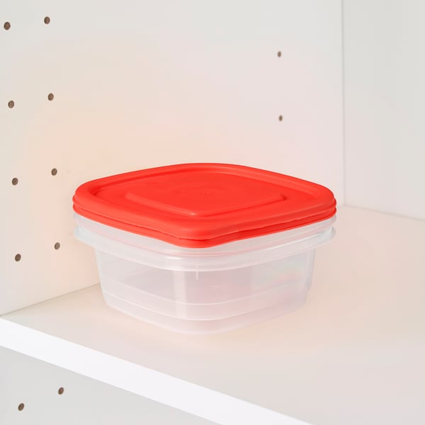A clear plastic food container with a bright red lid sits on a white shelf. Its stacked and stored efficiently, ideal for saving space.