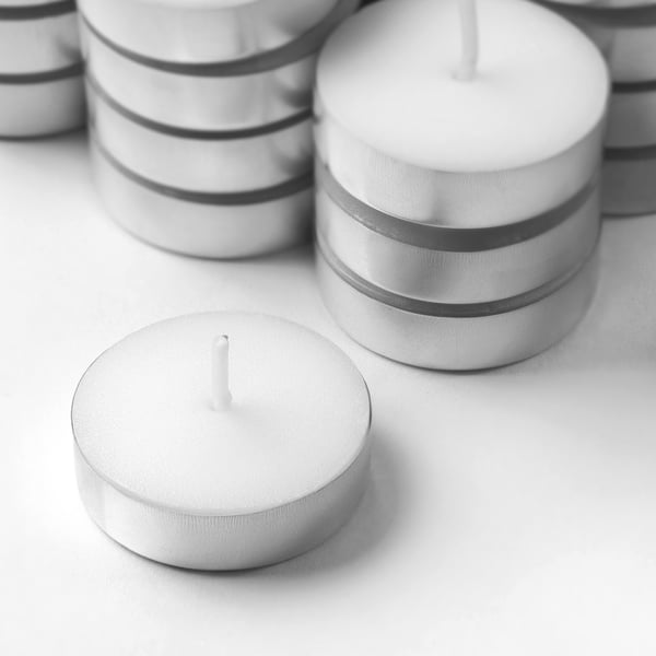 Multiple white tealights in metallic holders are neatly stacked; one is placed alone in the foreground, showcasing quality and simplicity.