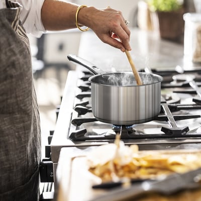 Cooking on gas stove with stainless saucepan, steam rising.