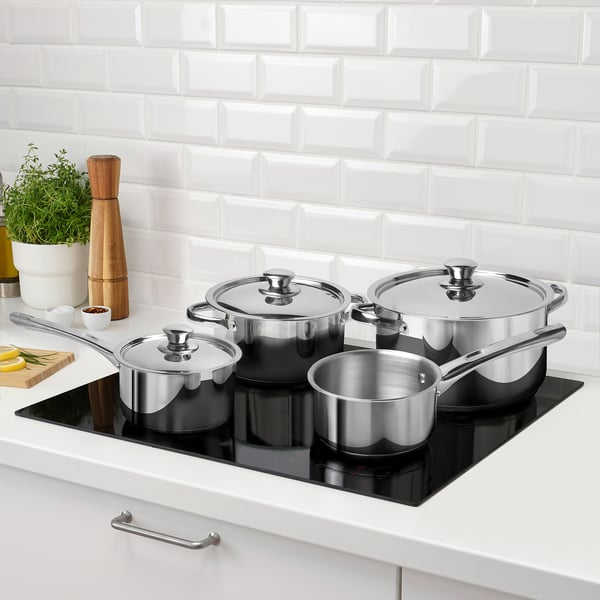 Four stainless steel pots/pans on black induction cooktop, all hob types, with lids.