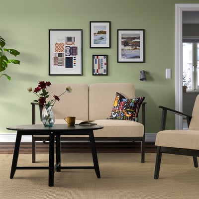 Retro living room with beige sofa, two armchairs, black coffee table, flowers, art, plant, doorway.
