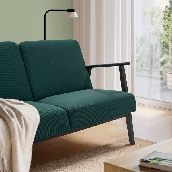 Dark green retro-style sofa with wooden legs, positioned near a window with sheer curtains.