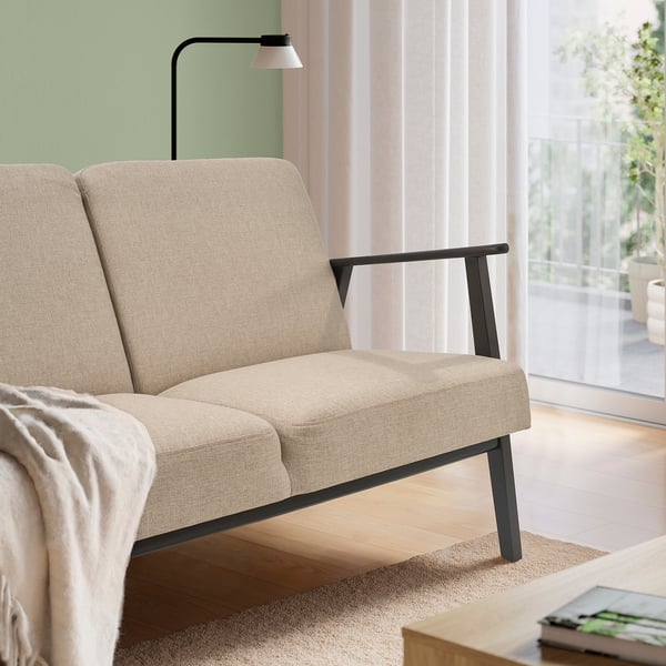 Beige sofa with dark wooden legs and high back. Against green wall, with lamp and light floor.