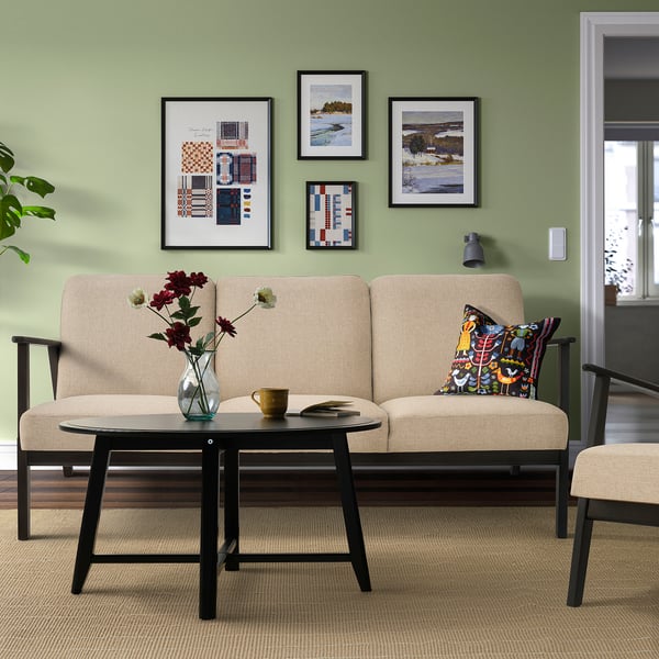 Modern living room with beige sofa, dark wood, colourful pillows, black coffee table, floral vase, art, green wall.