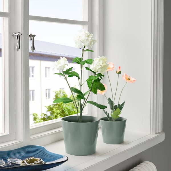 Two potted artificial flowers on a windowsill, brightening a room with lush greenery and blooms.