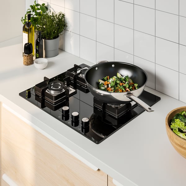Black FÖRBRÄNNA gas cooktop with large wok burner and colourful stir-fry. Sleek design in modern kitchen.