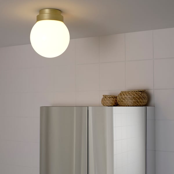 Bright, round ceiling light hangs above a metallic refrigerator, illuminating the area with soft, diffused light.