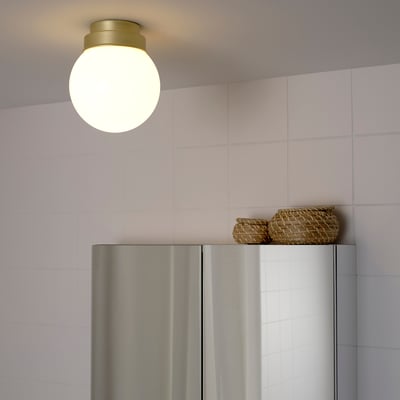 Bright, round ceiling light hangs above a metallic refrigerator, illuminating the area with soft, diffused light.