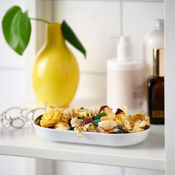 White bowl with yellow and brown potpourri on shelf, yellow vase, glass bottles.