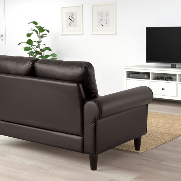 A modern living room with a black leather GAMMALBYN sofa, tv, and plant.