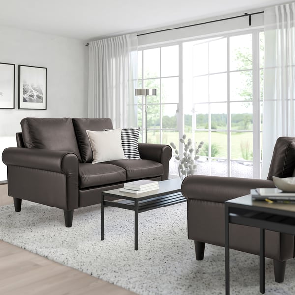 Modern living room with GAMMALBYN leather sofa, ottoman, glass coffee table, and large window with curtains. Light rug enhances space.