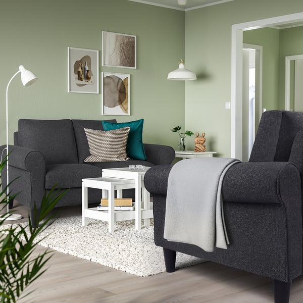 Modern living room with grey sofa & armchair, black/white pillows, blue cushion, green walls, white table & rug, hanging lamps, art, plant.