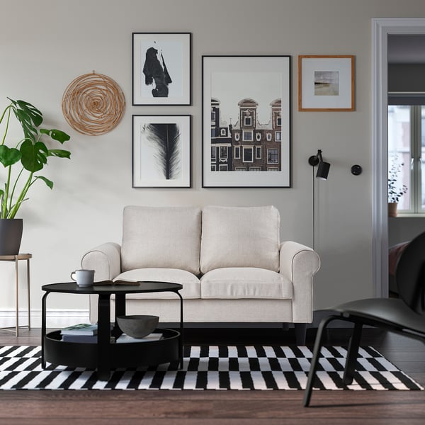 Modern living room with white GAMMALBYN sofa, black coffee table, monochrome rug, wall art, and plants.