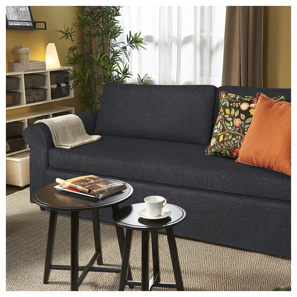 Modern living room with dark blue GAMMALBYN sofa-bed, pillows, side tables, and plants.
