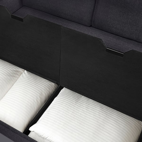 Modern sofa-bed with dark grey upholstery, white pillows, and built-in headrests. Suitable for small spaces with hidden storage.