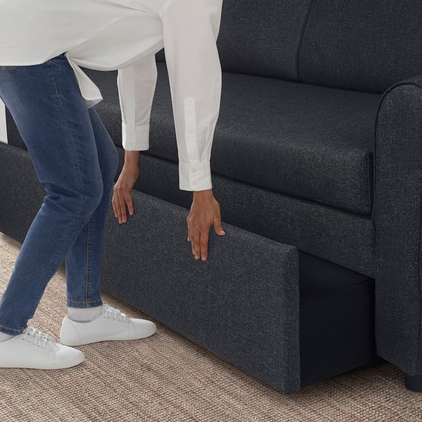 Person bends down to access GAMMALBYN sofa-beds under-seat storage, demonstrating its functionality and space-saving feature.