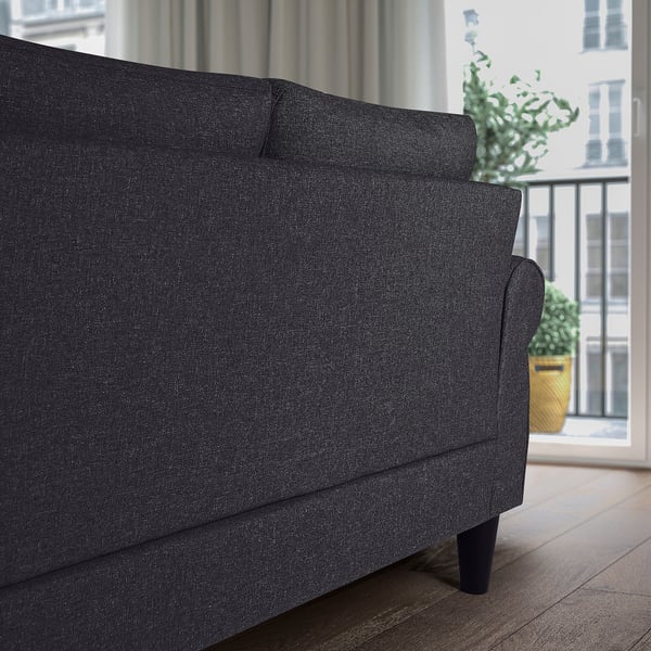 Dark grey upholstered sofa-bed near window with plants. Cushions visible, storage suggested.