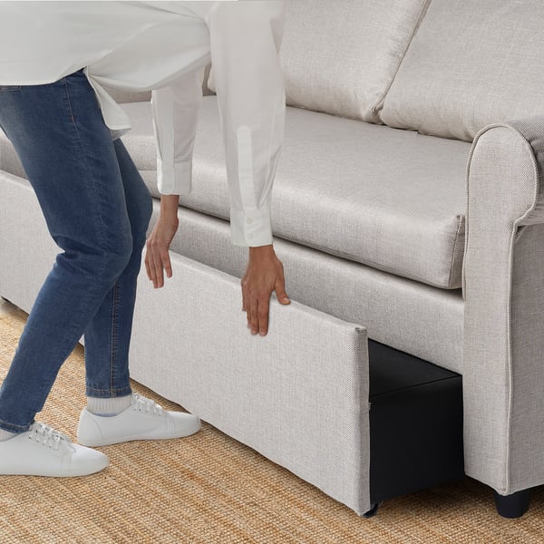 Person lifting seat of GAMMALBYN sofa-bed, revealing storage space for bedlinens.