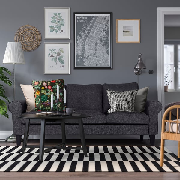 Cosy modern living room with dark grey GAMMALBYN sofa, patterned cushions, black coffee table, striped rug, colourful wall art, and grey lamp.