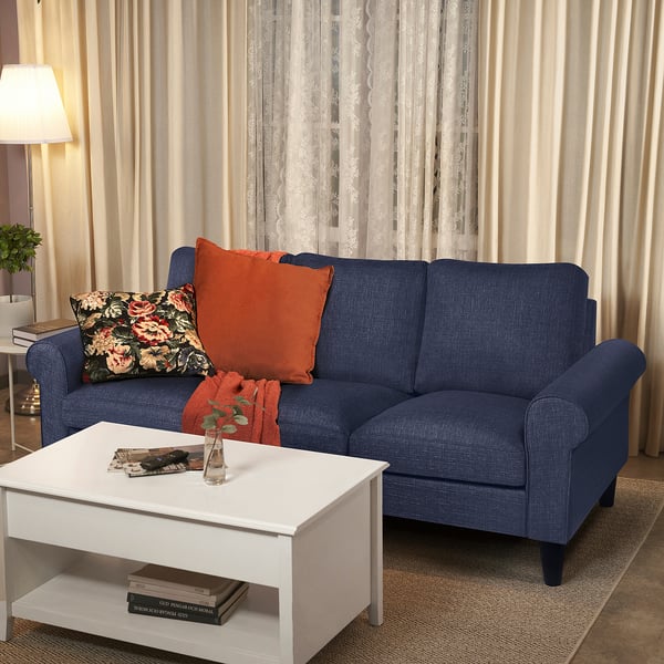 Blue GAMMALBYN sofa with orange pillows; white coffee table, books, and vase.