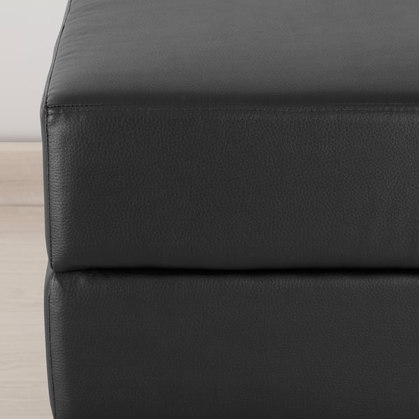 Black footstool with thick cushion, sturdy stitching, ideal for seating or resting feet.